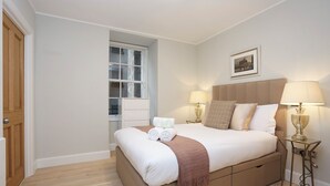 A neatly arranged bedroom with a bed, bedside lamps, a window, and a framed picture on the wall. - JOIVY Newly Refurbished Apartment on the Historic Royal Mile (Edinburgh)