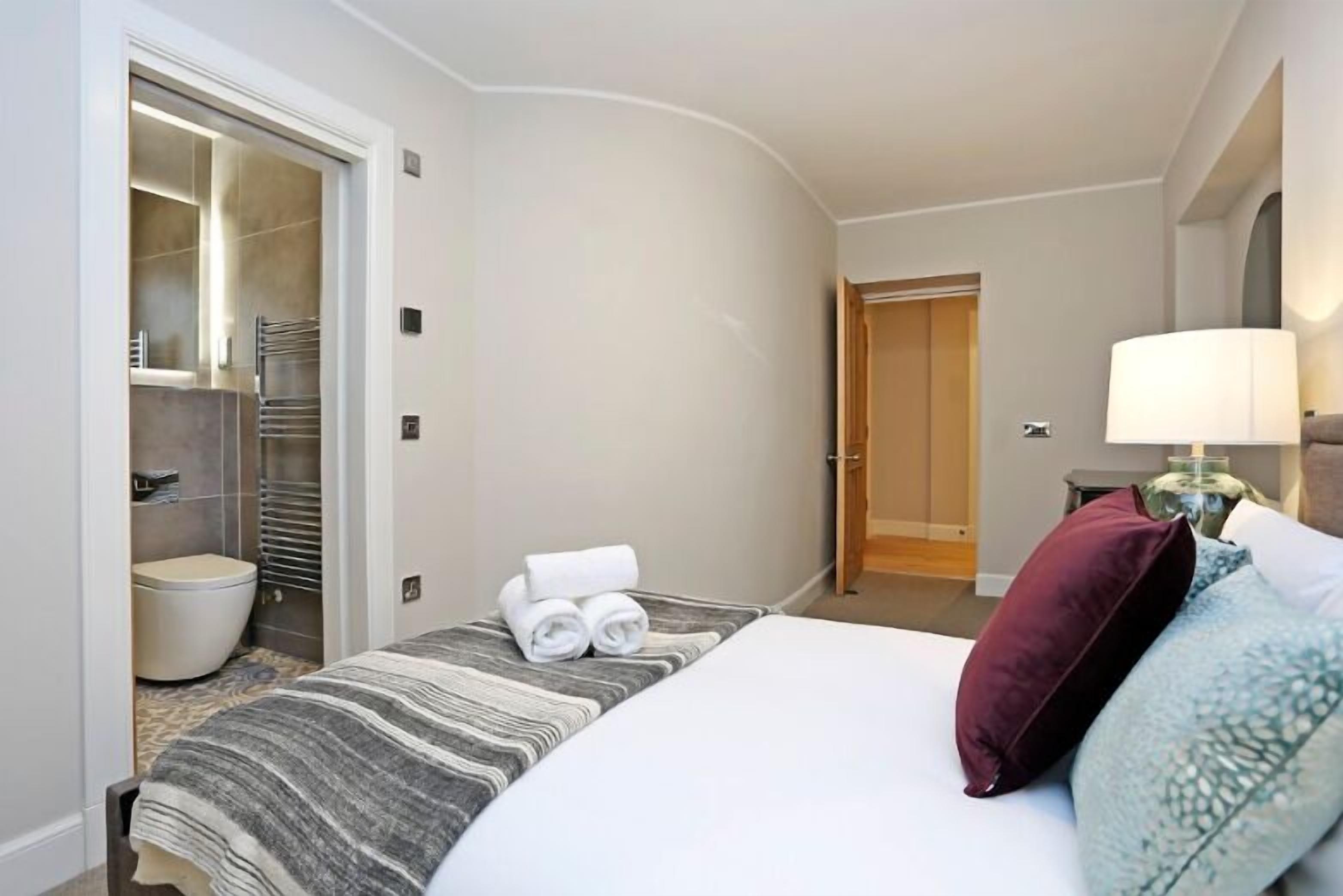 A hotel room with a bed, a bathroom with a toilet and towel rack, and a nightstand with a lamp.