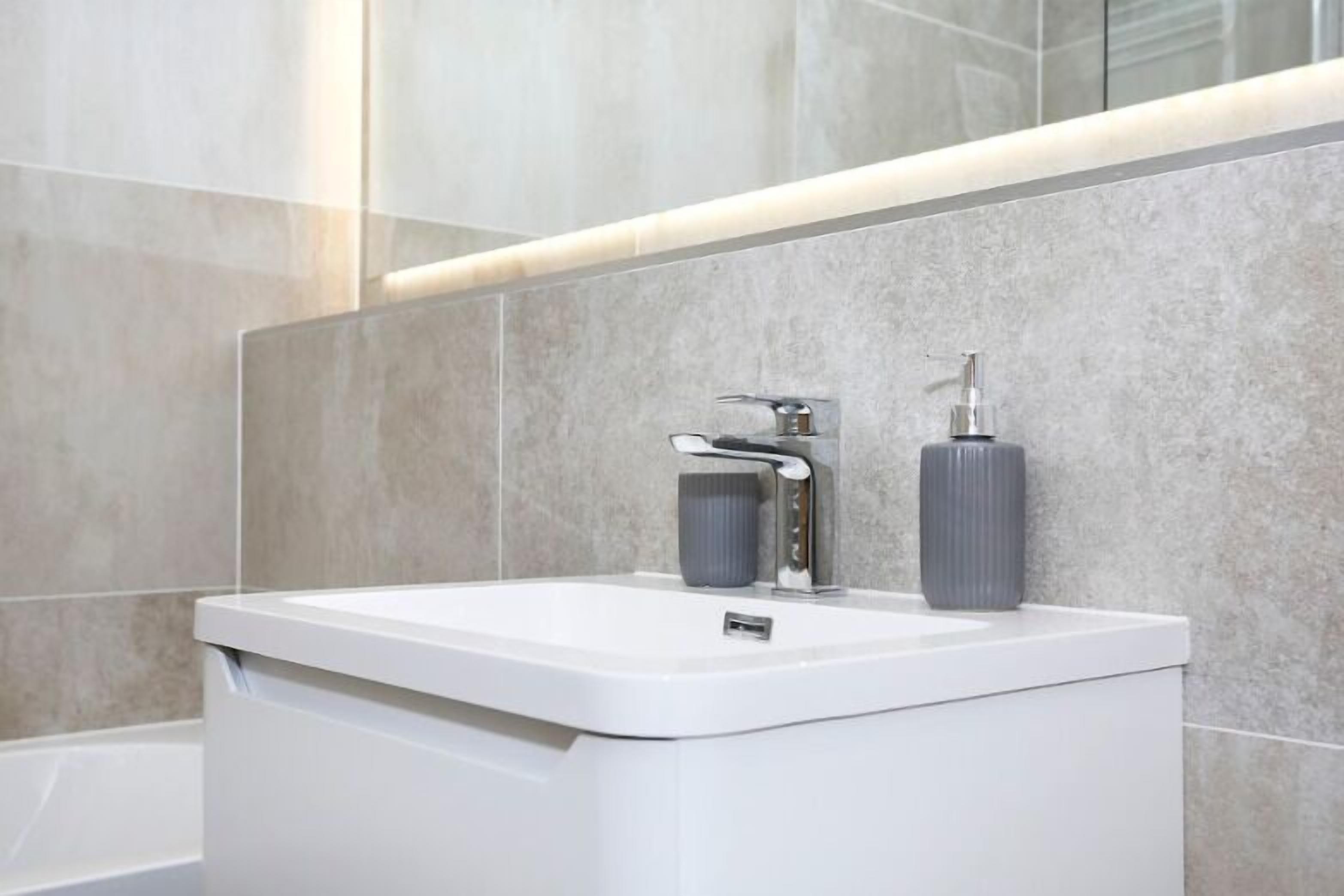 Un bagno moderno con lavandino bianco, rubinetto e dispenser di sapone.