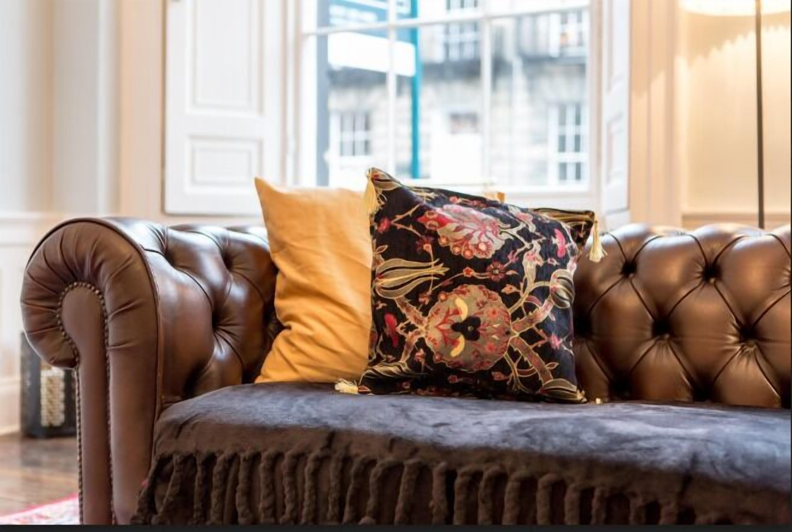 A brown leather sofa with a dark cushion and two decorative pillows, one yellow and one with a floral pattern.