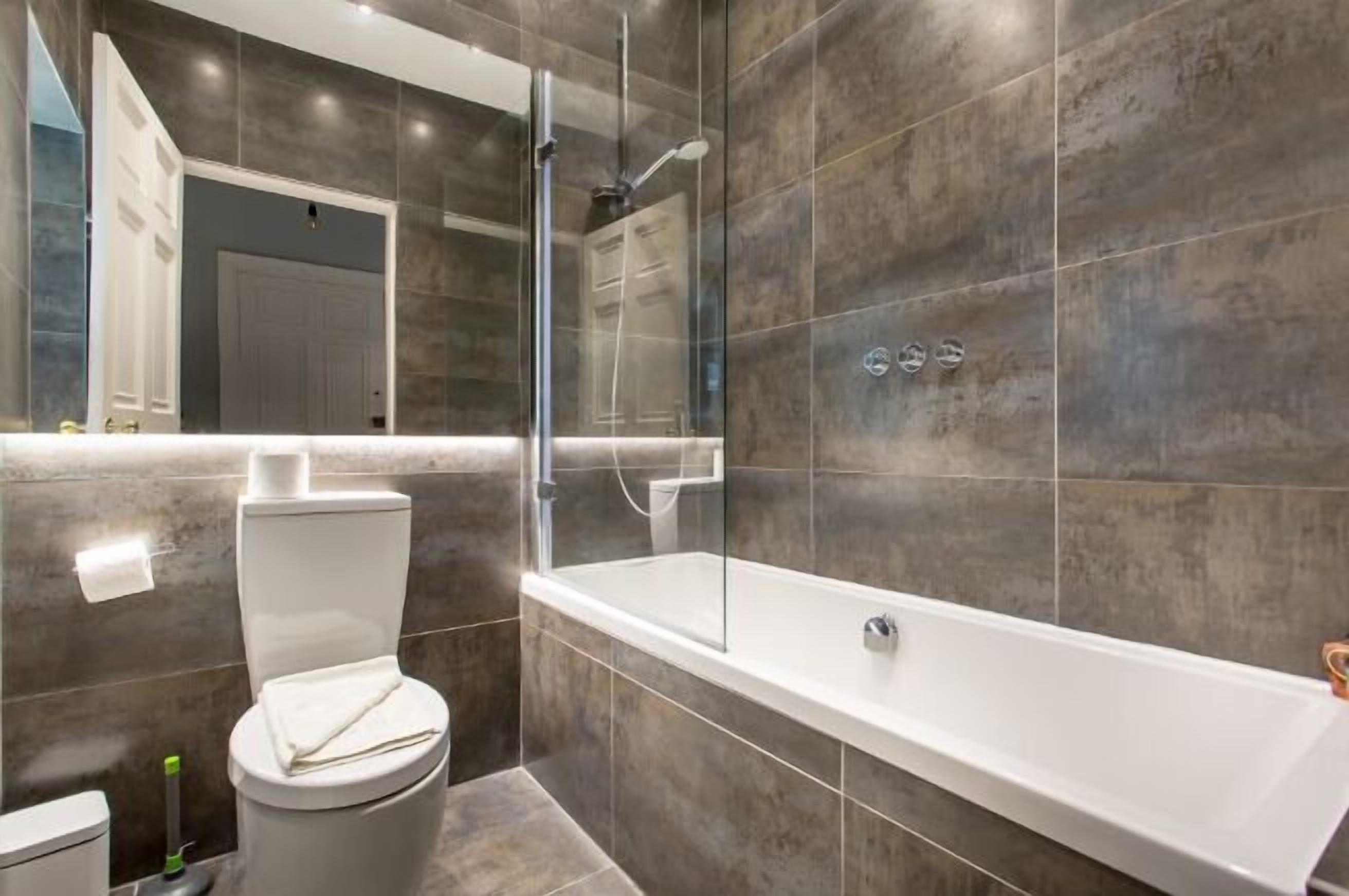 Un bagno moderno con doccia vetrata, una vasca da bagno bianca e un water.