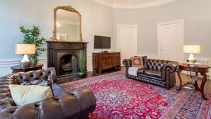 A living room with a fireplace, leather sofas, a large mirror, and a chandelier. - JOIVY Converted Flat in Historic Building in Desirable New Town (Edinburgh)