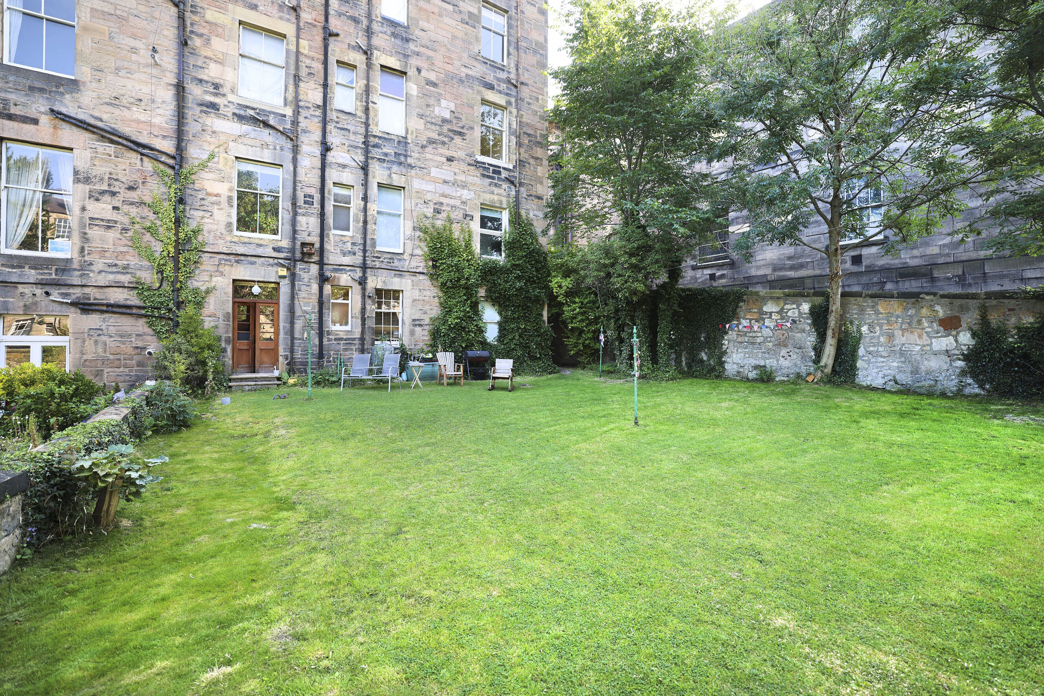 A courtyard with a grassy lawn, a stone building with multiple windows, and a tree.