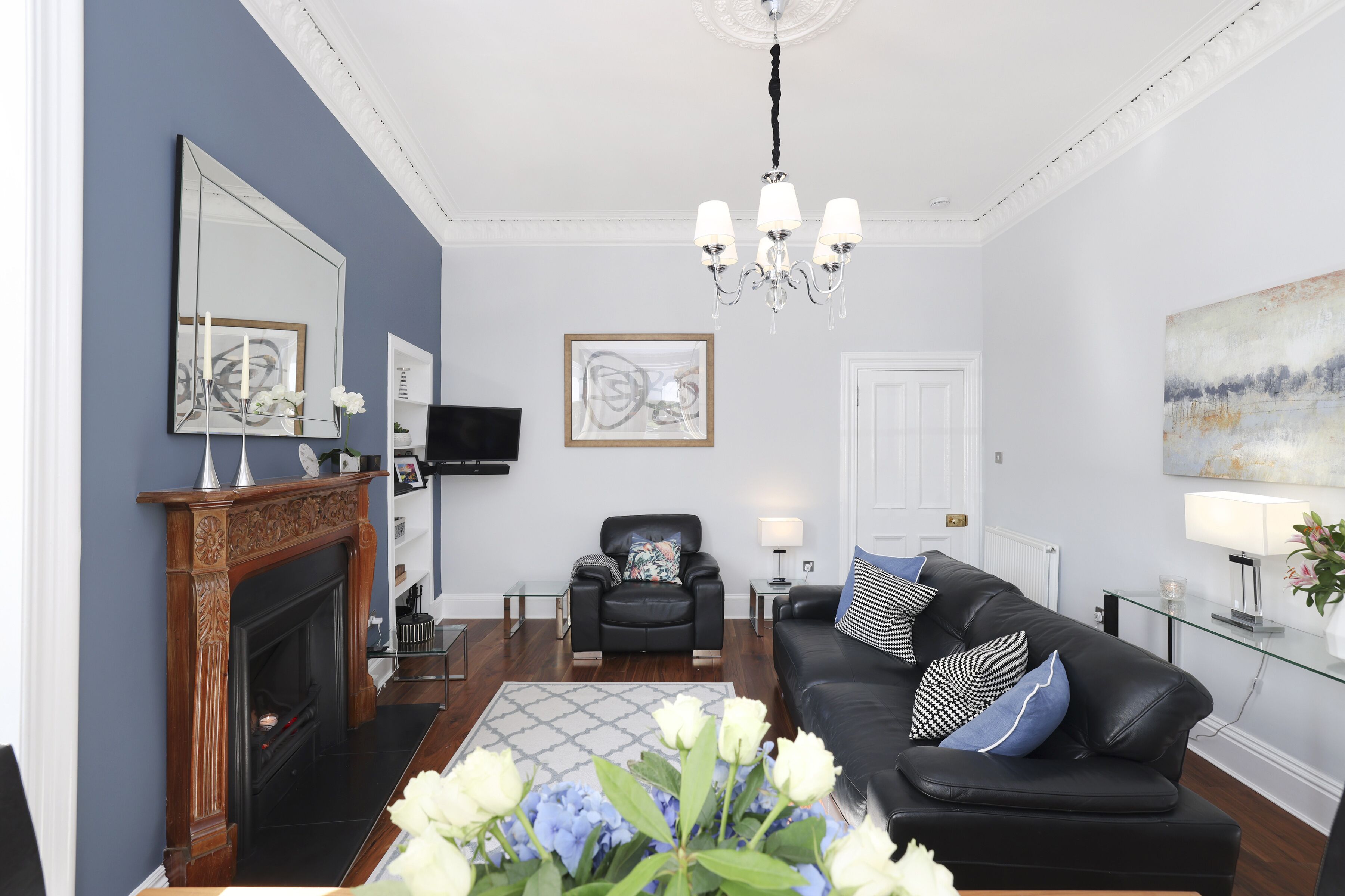 A living room with a fireplace, a black leather sofa, a glass coffee table, and a chandelier.