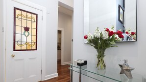 A hallway with a white door, a glass shelf with a vase of flowers, and a mirror on the wall. - JOIVY Stunning Ground-floor 2bedrm New Town Apt (Edinburgh)