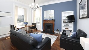A living room with a fireplace, a dining area, and a seating area with a sofa and armchair. - JOIVY Stunning Ground-floor 2bedrm New Town Apt (Edinburgh)