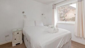 A white bedroom with a single bed, a bedside table, a nightstand, and a window with curtains. - JOIVY Heart of The Royal Mile (Edinburgh)
