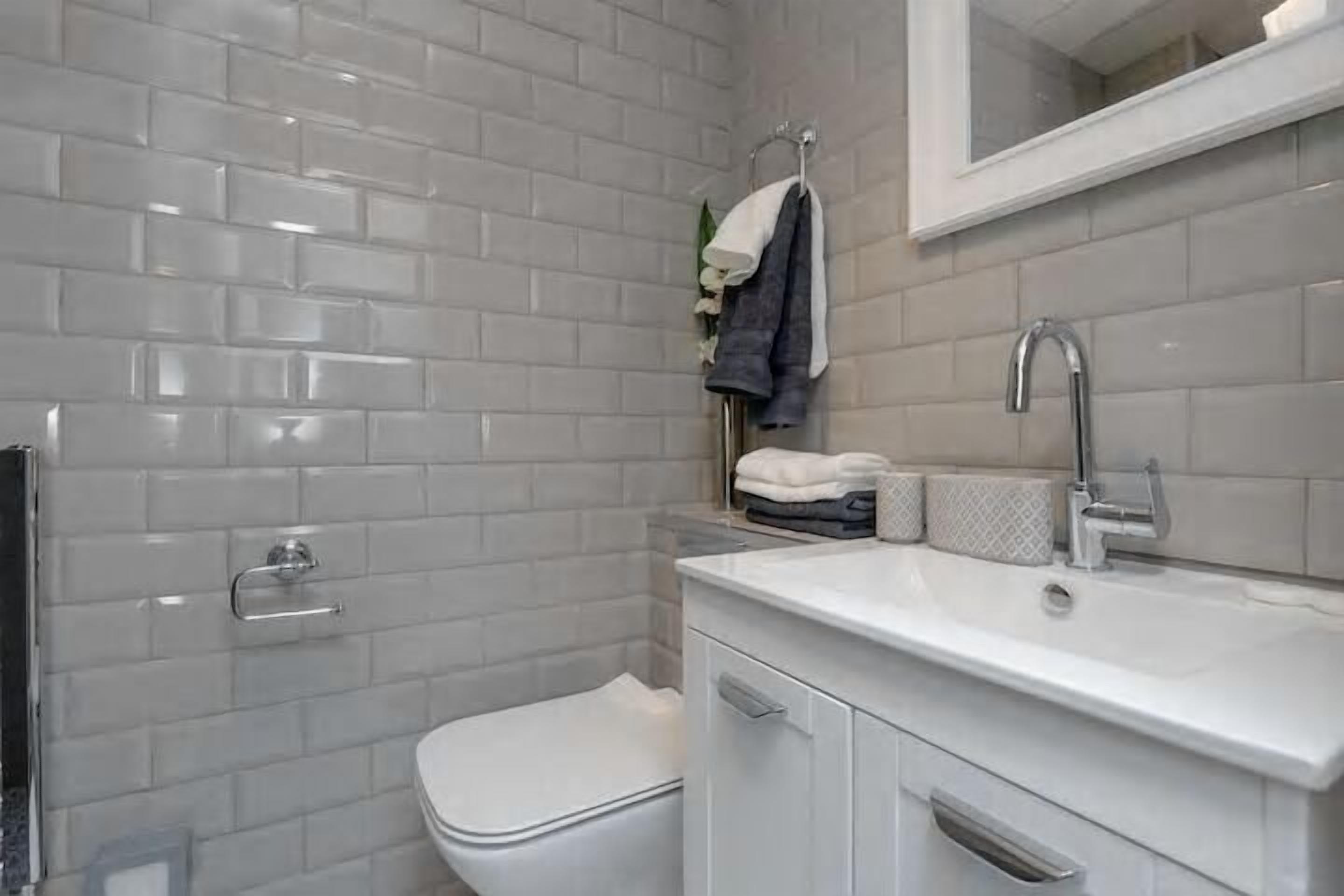 A bathroom with white subway tiles, a white sink, and a toilet.