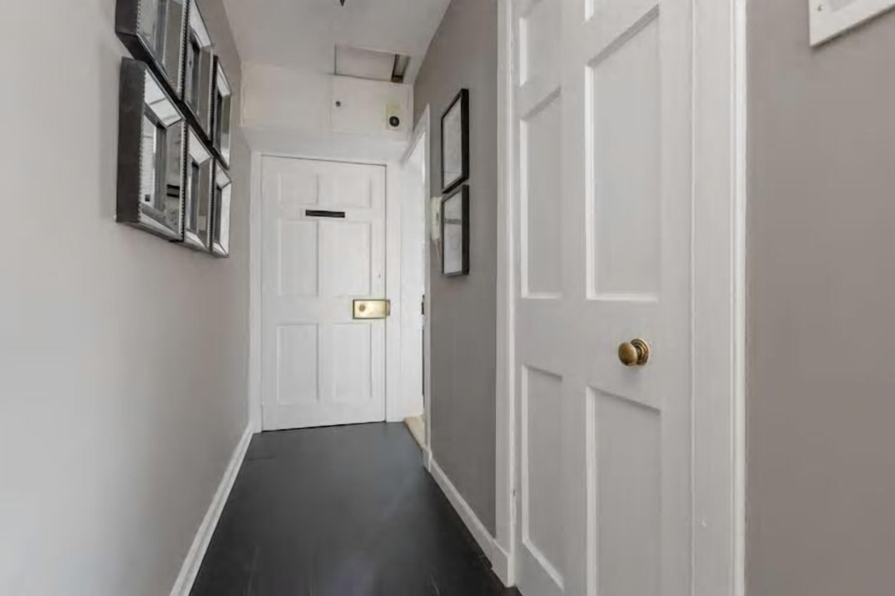 A hallway with a white door, a black floor, and a wall-mounted mirror.