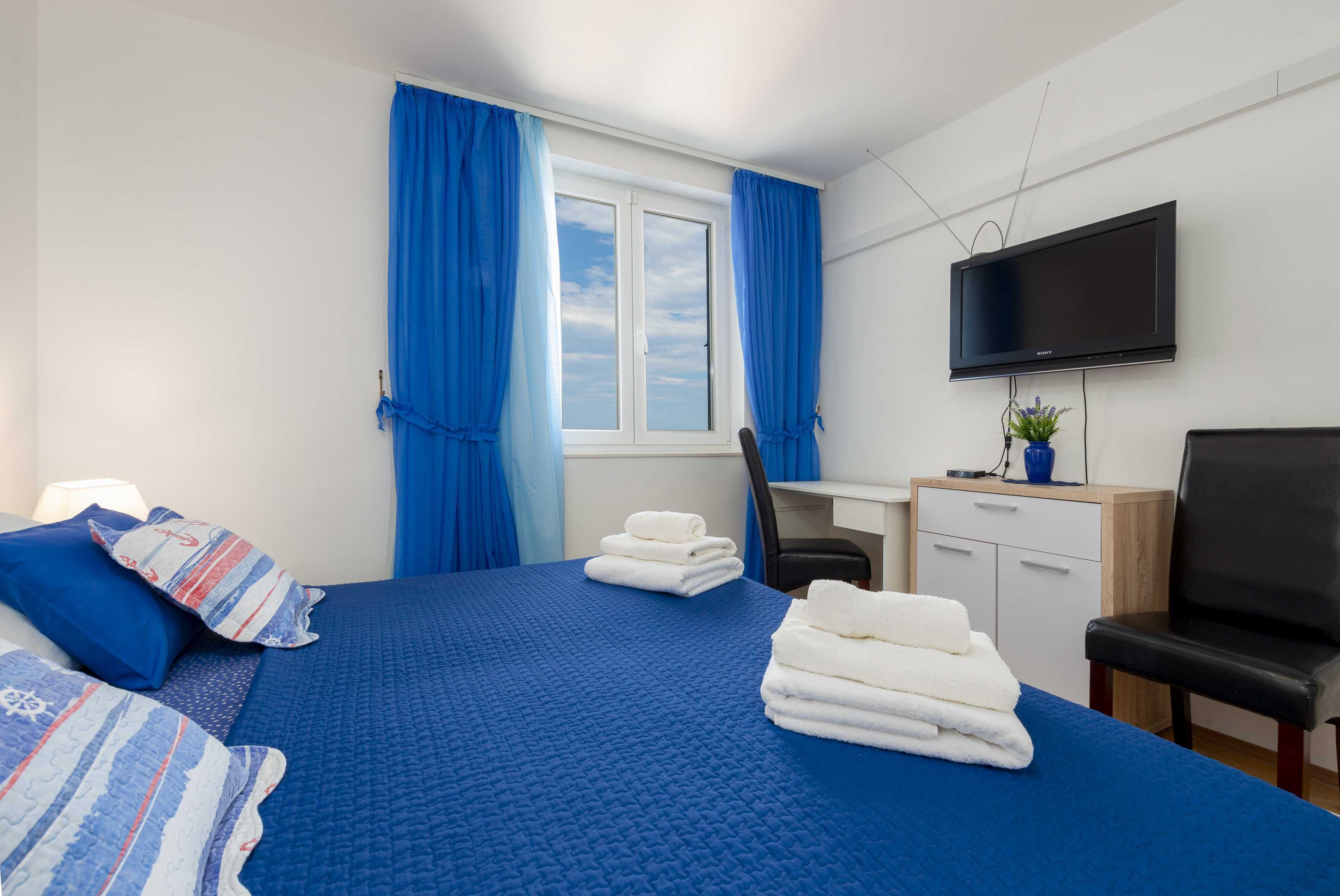 A hotel room with a bed, a desk, a chair, a TV, and a window with curtains.