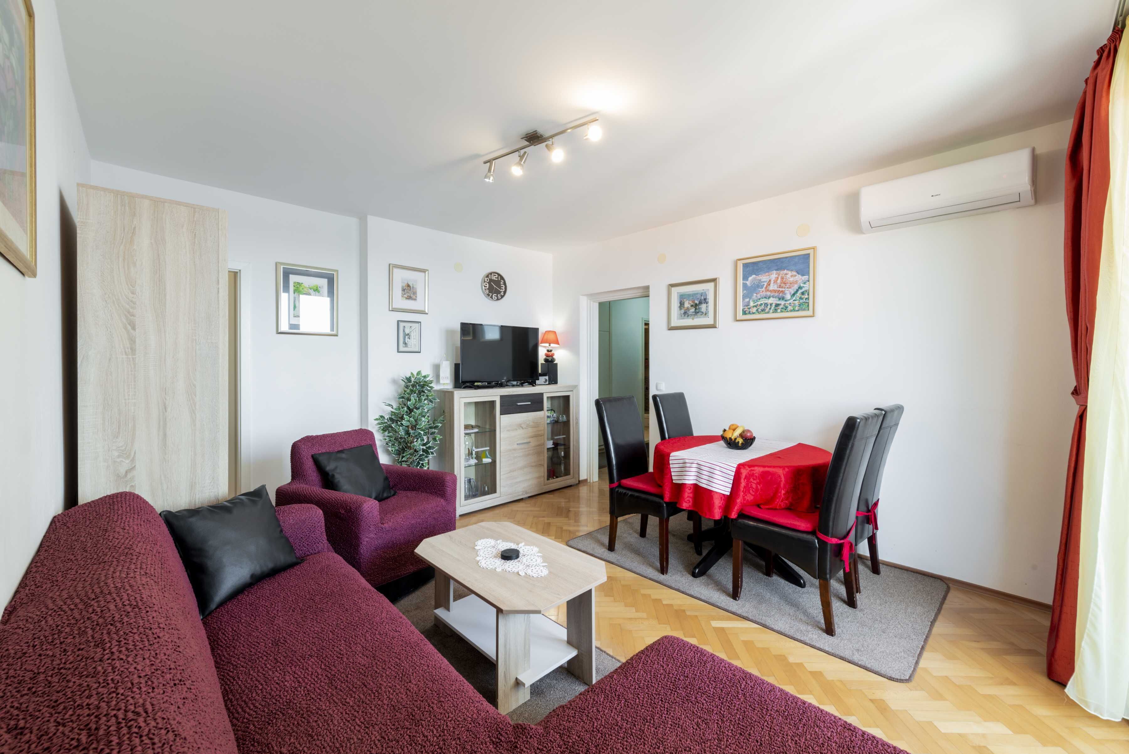 A living room with a sofa set, a dining table with chairs, a TV, and a small table with a decorative item.