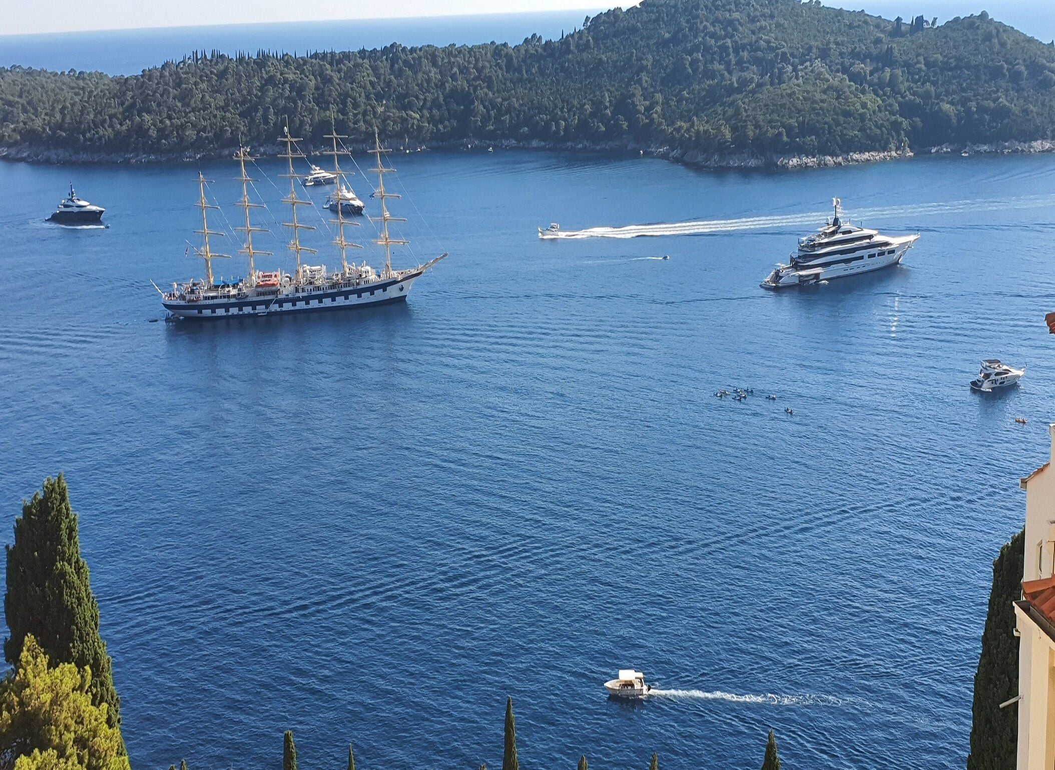 A coastal scene with multiple boats, including a large sailing ship and a yacht, on a calm sea.