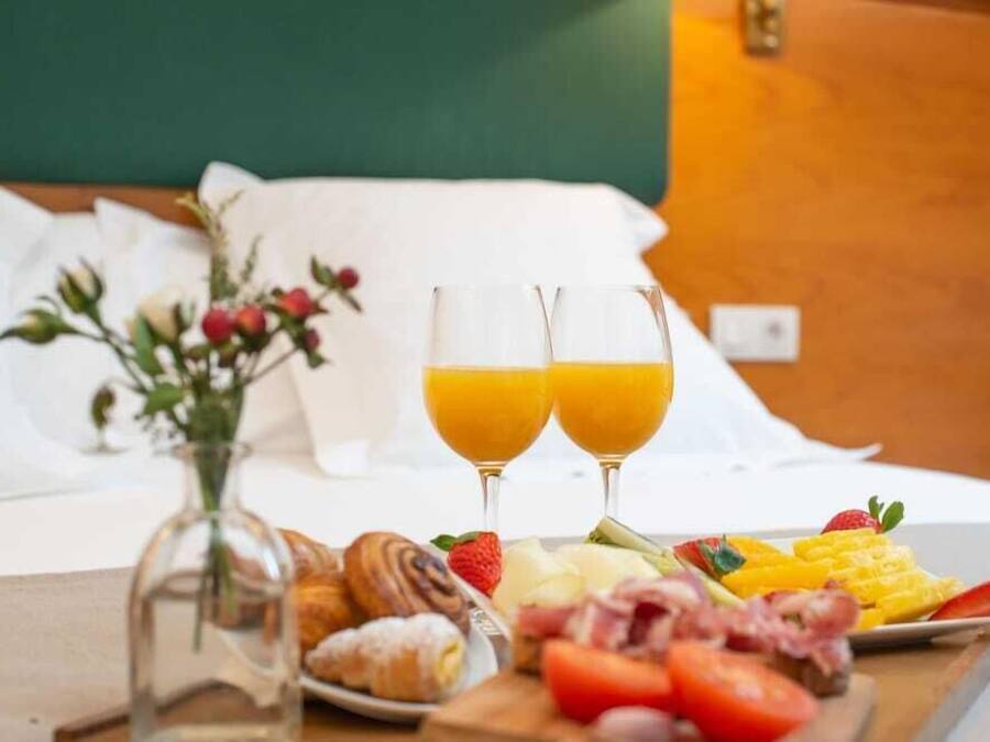 Une table en bois dressée pour le petit-déjeuner, avec des croissants, des fraises, du fromage et du jus d’orange.