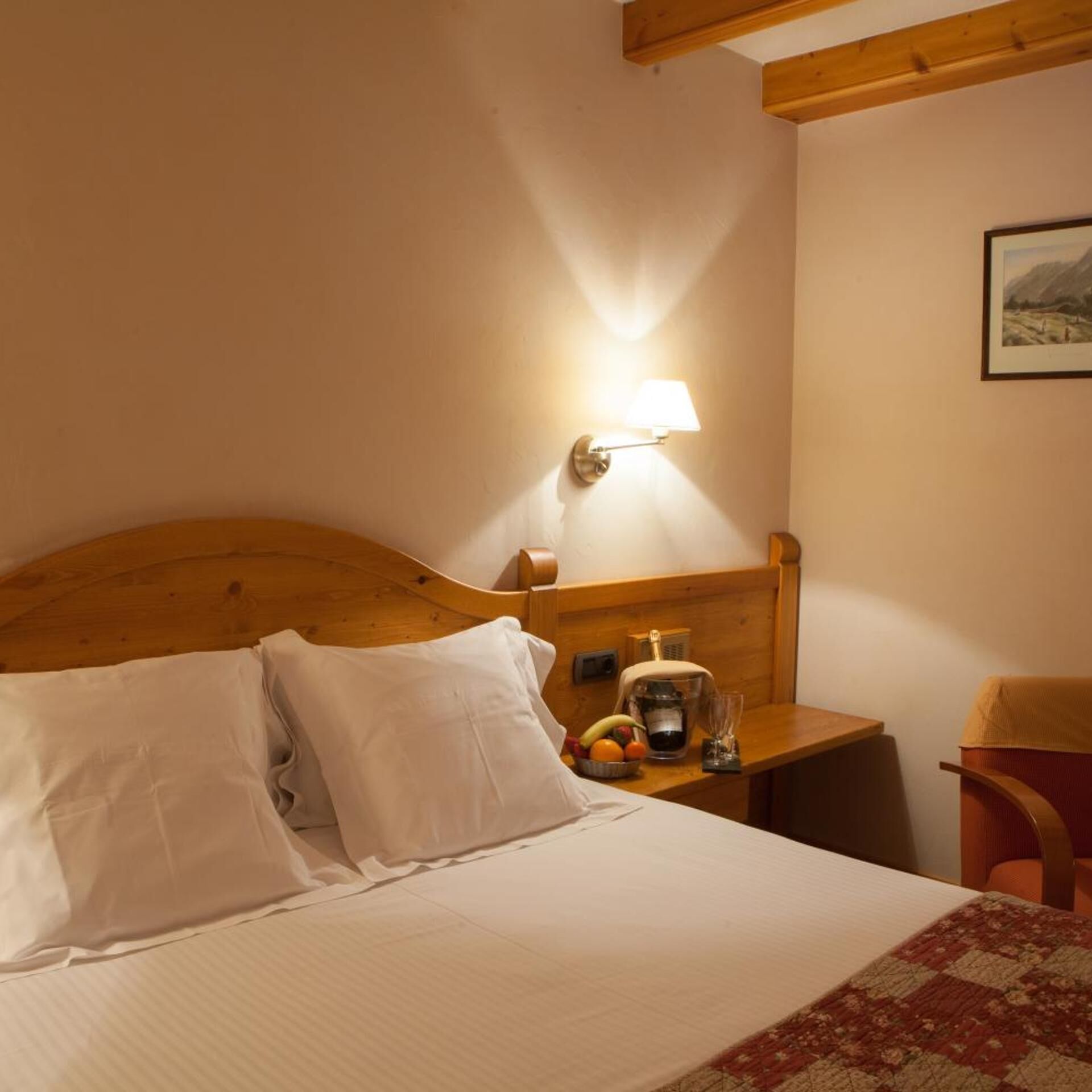 A hotel room with a wooden headboard, a bedside table with a lamp, a chair, and a bed with pillows.