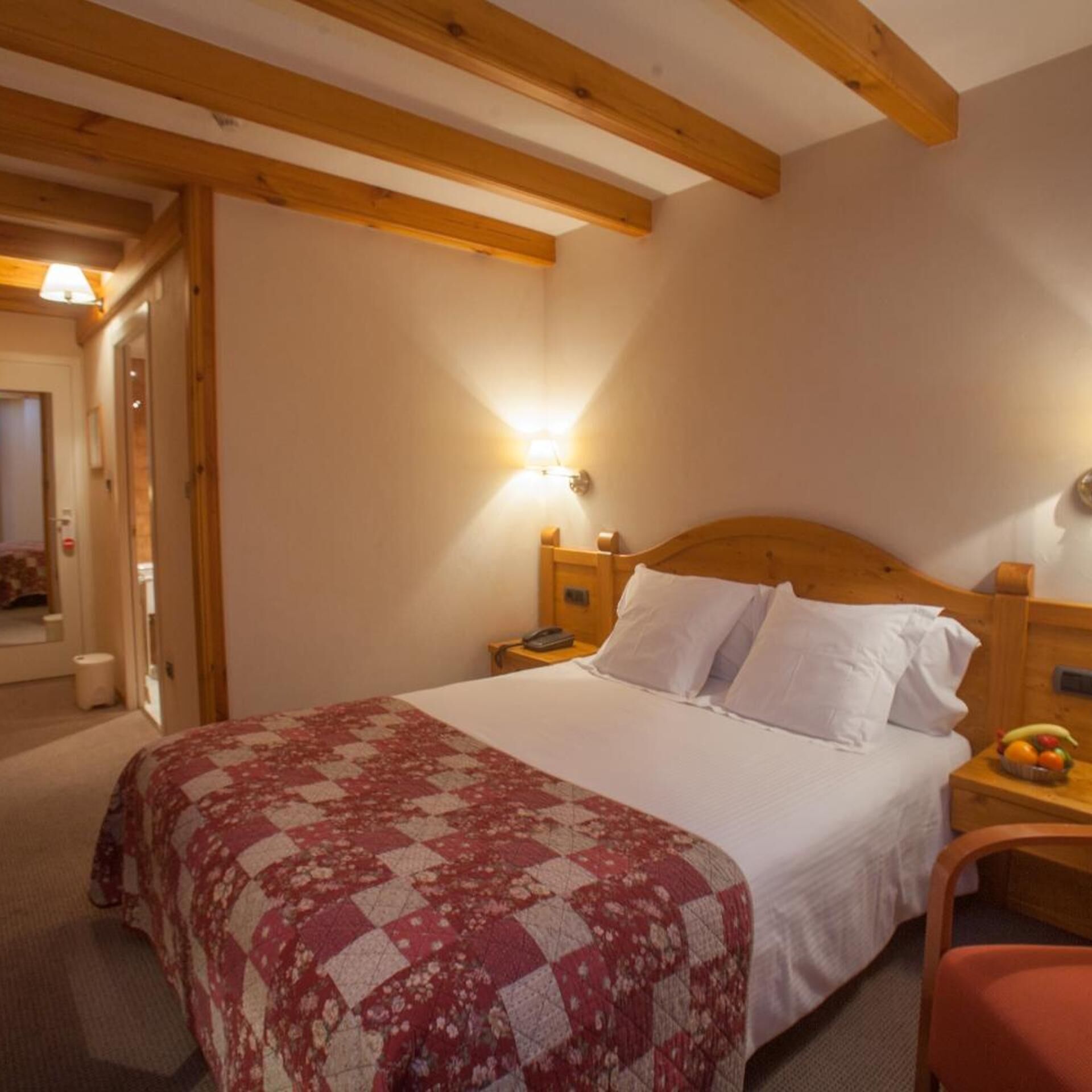 Une chambre à coucher avec une tête de lit en bois, un lit avec une literie blanche, une courtepointe, des tables de chevet avec des lampes et un panier de fruits sur la table de chevet.