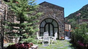 A stone building with a large arched window and a small patio with white chairs and a table. - Bonavida (Canillo)