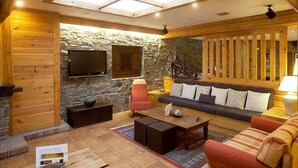 A cozy living room with a stone wall, wooden furniture, a flat-screen TV, and a wooden ceiling with skylights. - Bonavida (Canillo)