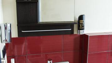 Un baño con lavamanos blanco, baldosas rojas, un espejo, dispensador de gel antibacterial y un cubo de basura.