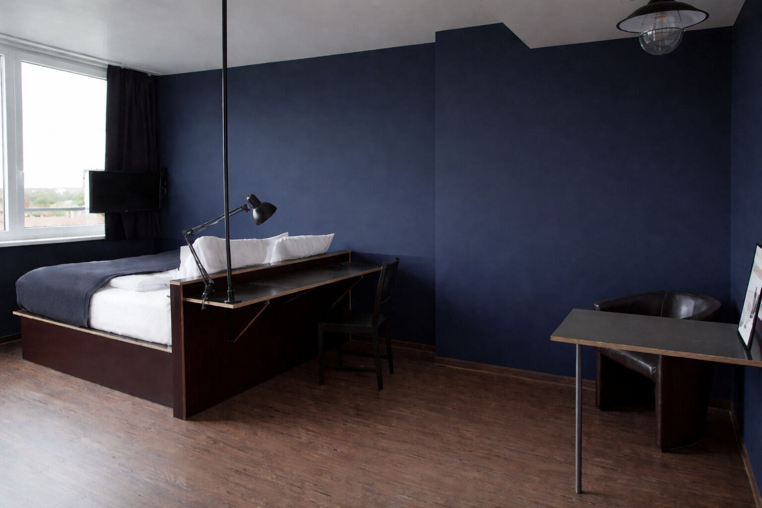 A bedroom with a bed, desk, chair, and a hanging lamp.