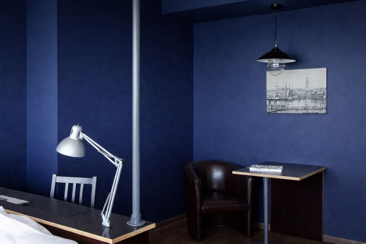 A room with a desk, chair, lamp, and a framed picture on the wall.