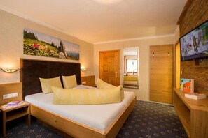 Quarto de hotel com uma cama grande, cabeceira de madeira, um quadro sobre a cama, uma televisão na parede e uma porta de madeira.