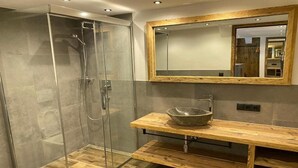 A modern bathroom with a glass-enclosed shower, a wooden vanity with a bowl sink, and a large mirror with a wooden frame. - Hotel Jagerhof (Kaunertal)