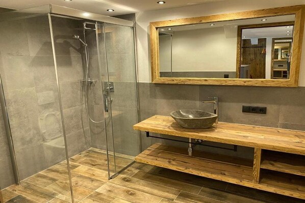 Une salle de bain moderne dotée d’une douche à parois de verre, d’un meuble-lavabo en bois avec un vasque et d’un grand miroir encadré en bois.