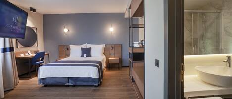 Una habitación de hotel con cama, escritorio, silla, televisor y baño con lavamanos y ducha.