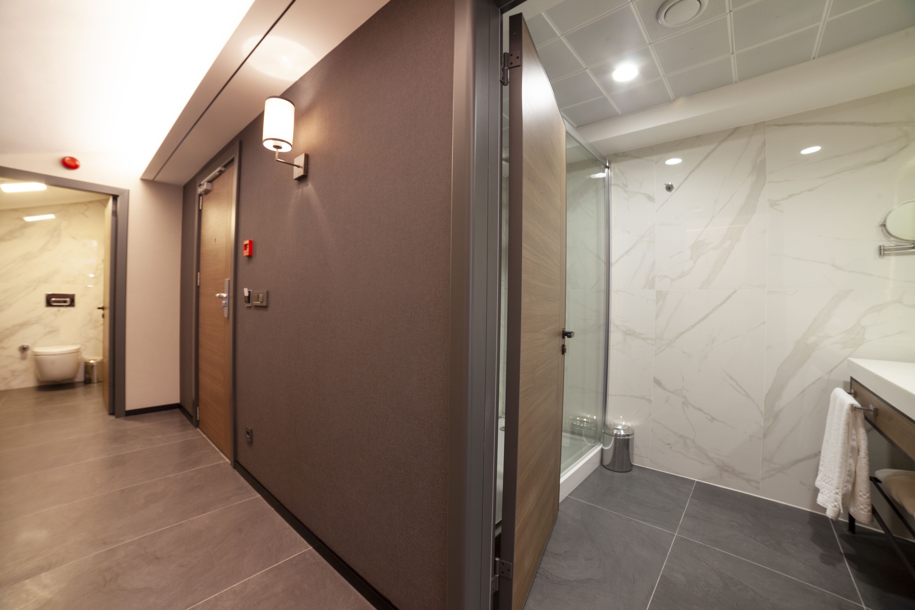 Un baño moderno con pared de mármol, cabina de ducha de vidrio y puerta de madera.