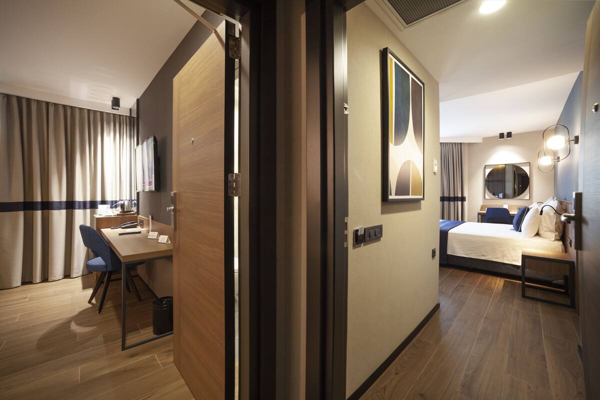 A hotel room with a desk, chair, bed, and a large mirror.