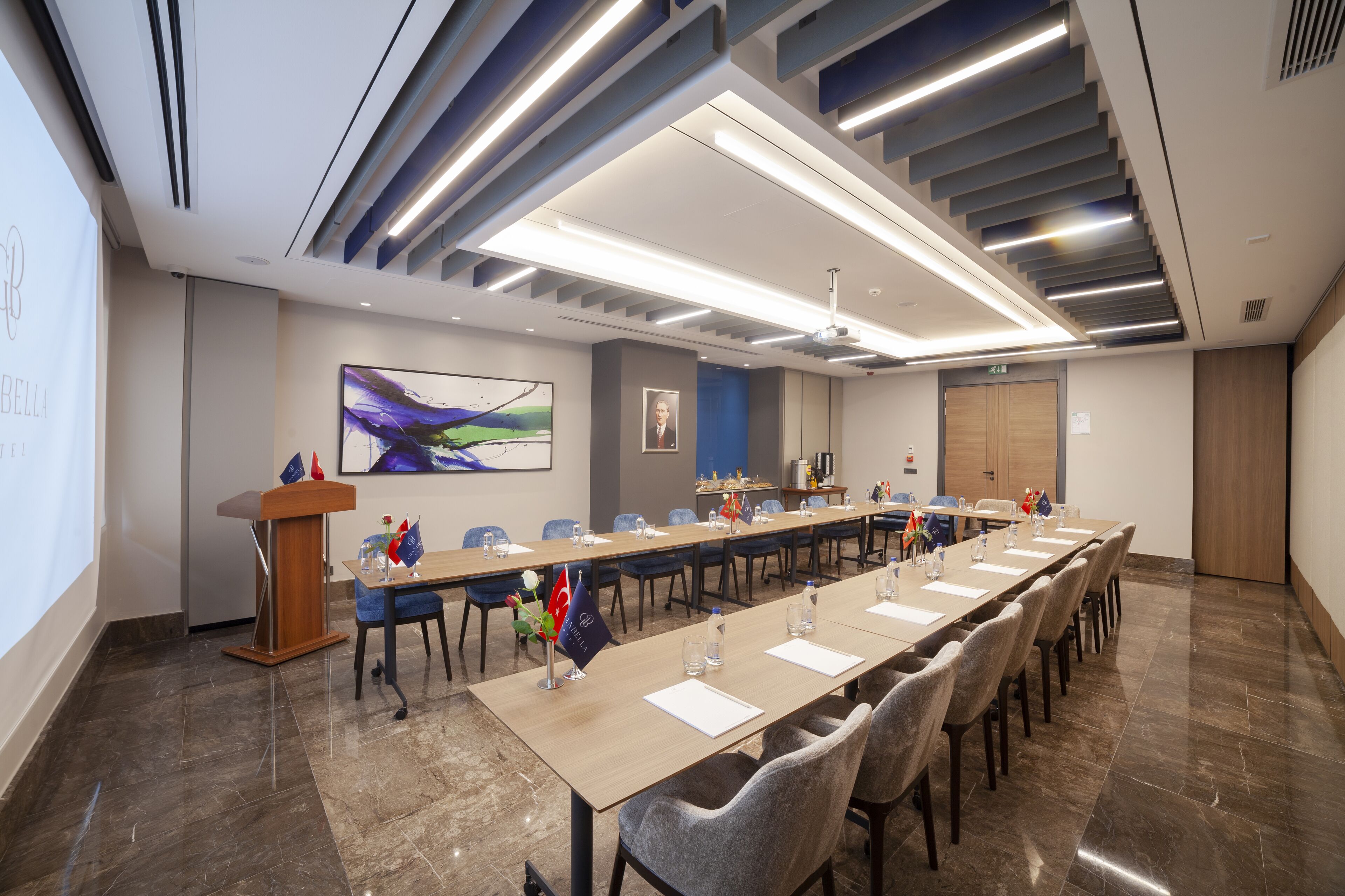 A conference room with a long table, chairs, a podium, and a projector screen.
