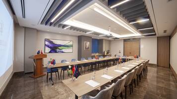 A conference room with a long table, chairs, a podium, and a projector screen.