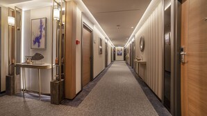 A hotel hallway with a carpeted floor, wooden doors, and a long corridor with framed artwork on the walls. - Granbella Hotel (Tekirdag)
