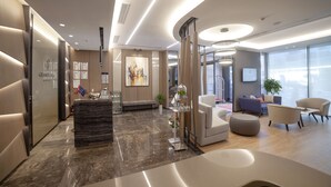 A modern hotel lobby with a reception desk, seating area, and large windows. - Granbella Hotel (Tekirdag)