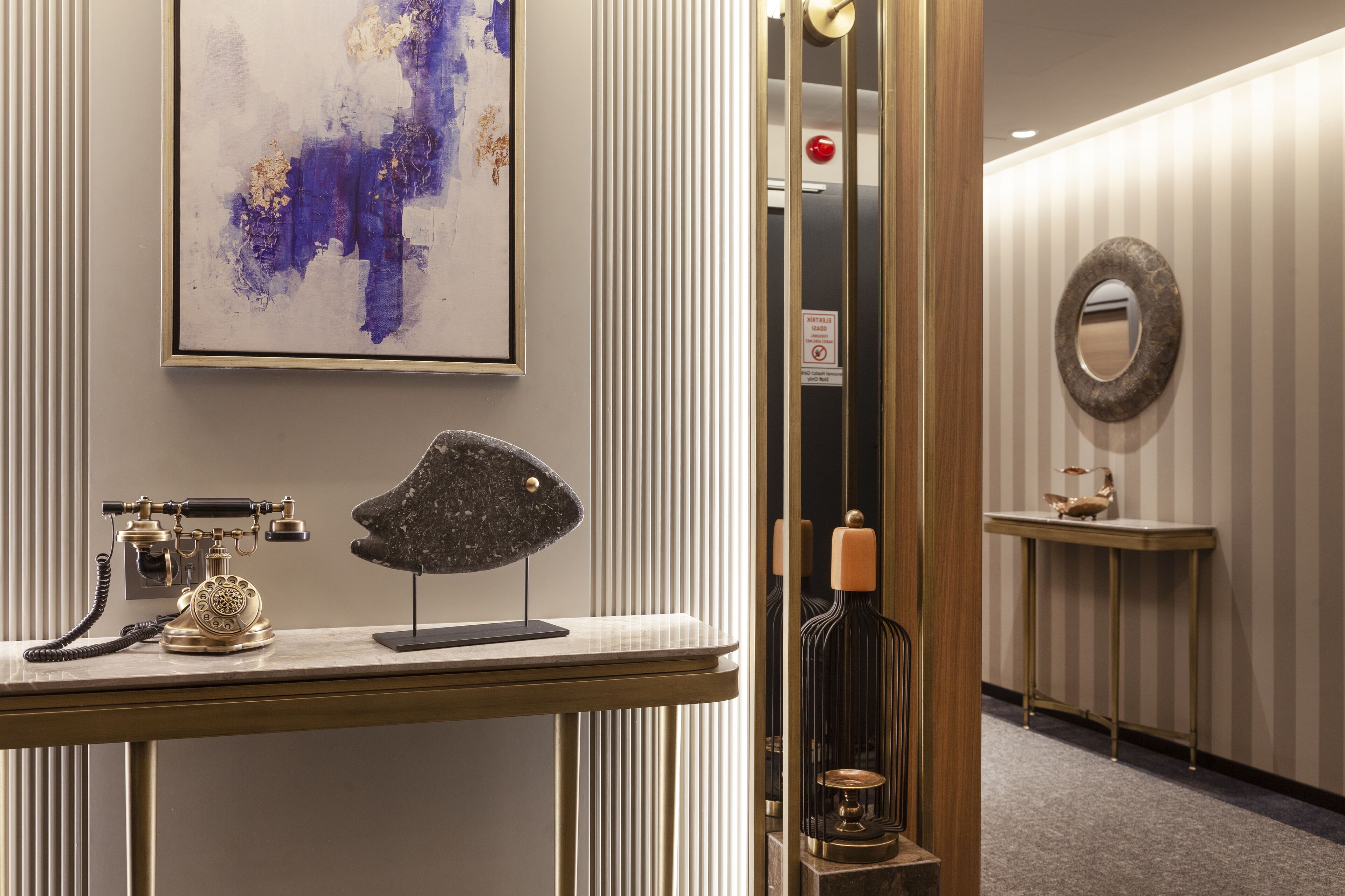 A modern hotel lobby with a reception desk, a telephone, a decorative sculpture, a mirror, and a wall-mounted sign.