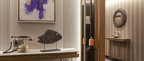 A modern hotel lobby with a reception desk, a telephone, a decorative sculpture, a mirror, and a wall-mounted sign.
