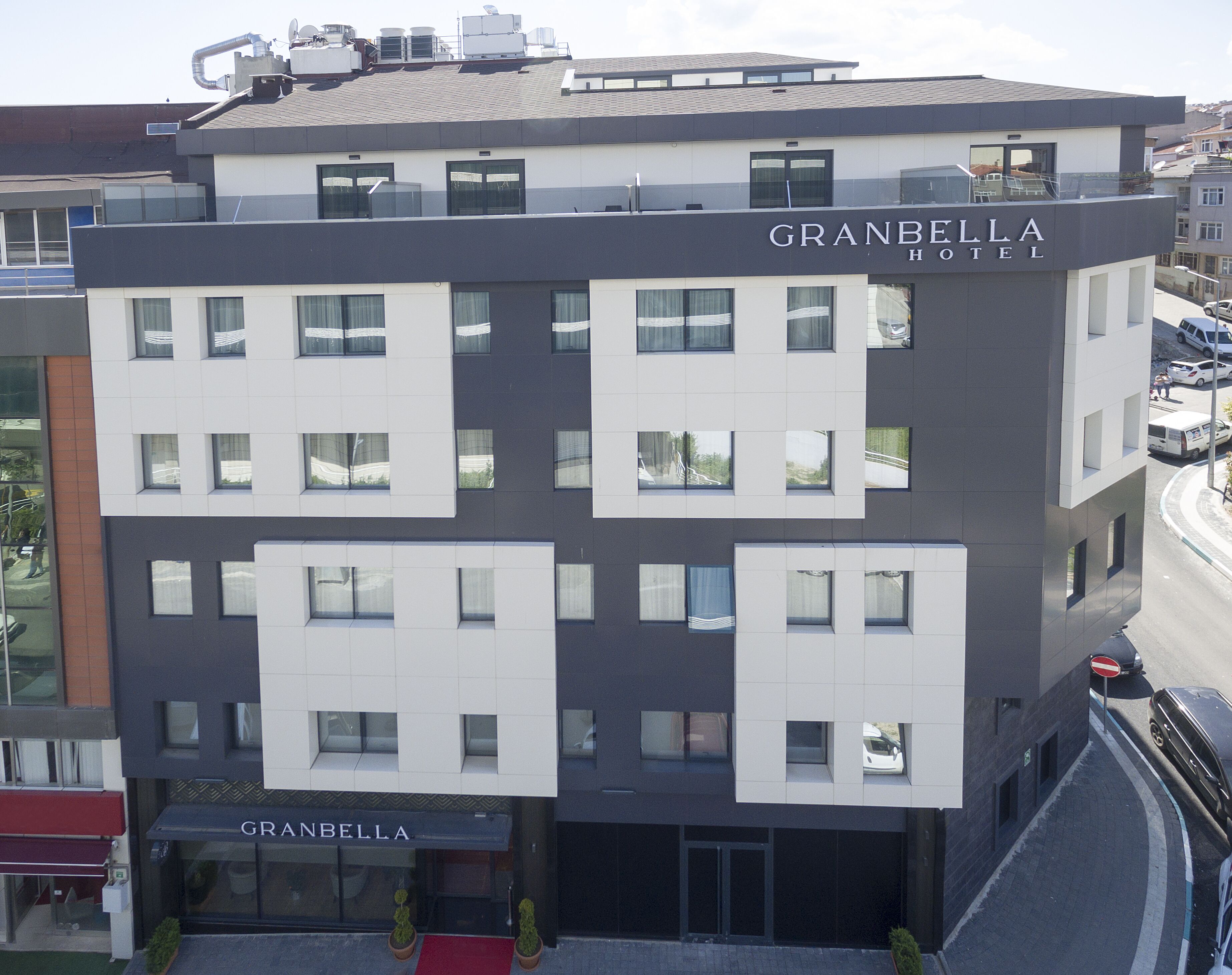 A modern hotel with a flat roof, multiple windows, and a sign reading "GRANBELLA HOTEL".