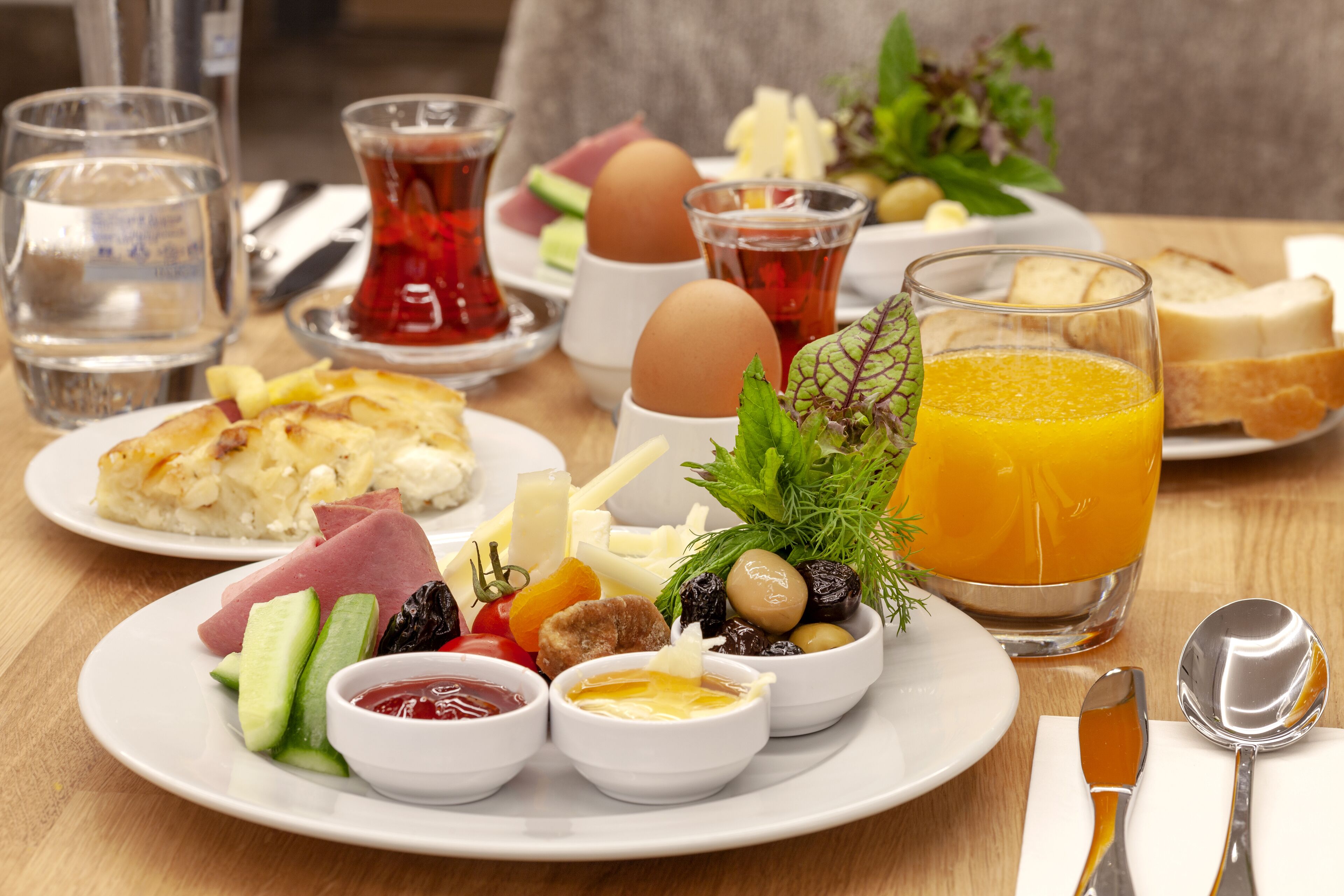 A breakfast setting with plates of food, glasses of water and tea, and a glass of orange juice.
