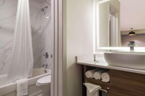 A bathroom with a bathtub, a toilet, a sink with a large mirror, and a shower with a curtain. - Signature Inn Houston Galleria (Houston)