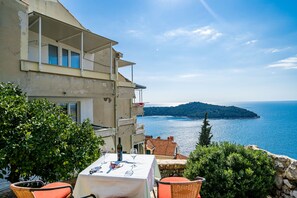 A balcony with a table set for dining, overlooking a coastal view with a clear sky. - Sea View Apartments - Lenka Radic Zlatni Potok 28 (Dubrovnik)