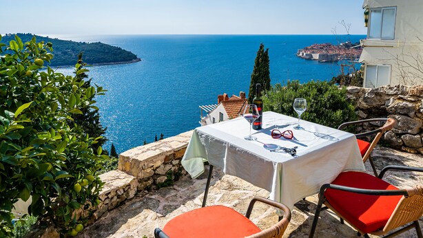 A table set outdoors with a view of the sea, stone walls, and a building in the background.