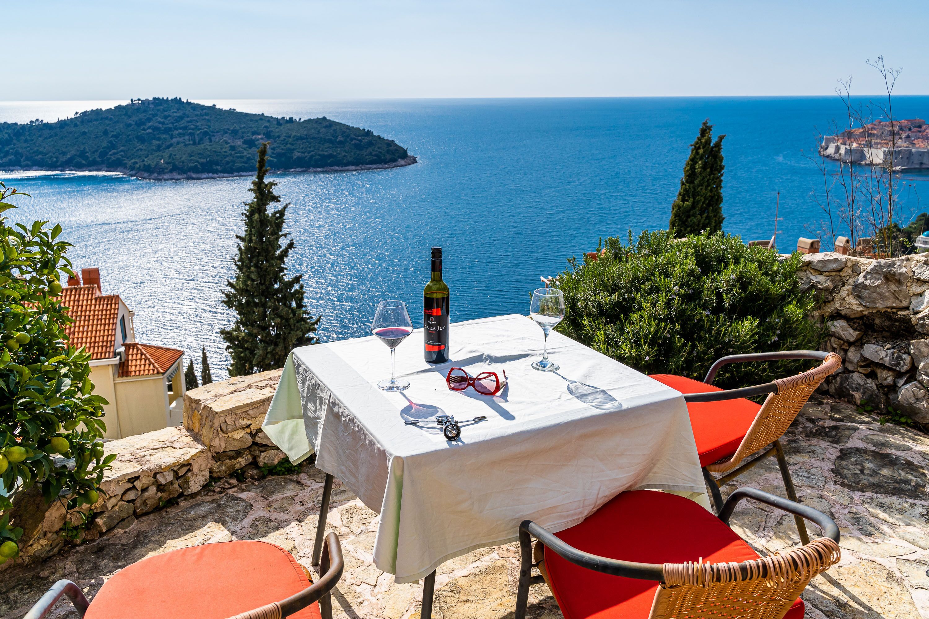 Ein Tisch für zwei, gedeckt mit Wein und Gläsern, mit Blick auf die Küste, eine entfernte Insel und felsiges Gelände.