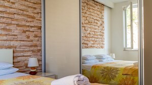 A hotel room with a stone wall, a bed with a floral bedspread, a bedside lamp, and a window with daylight.