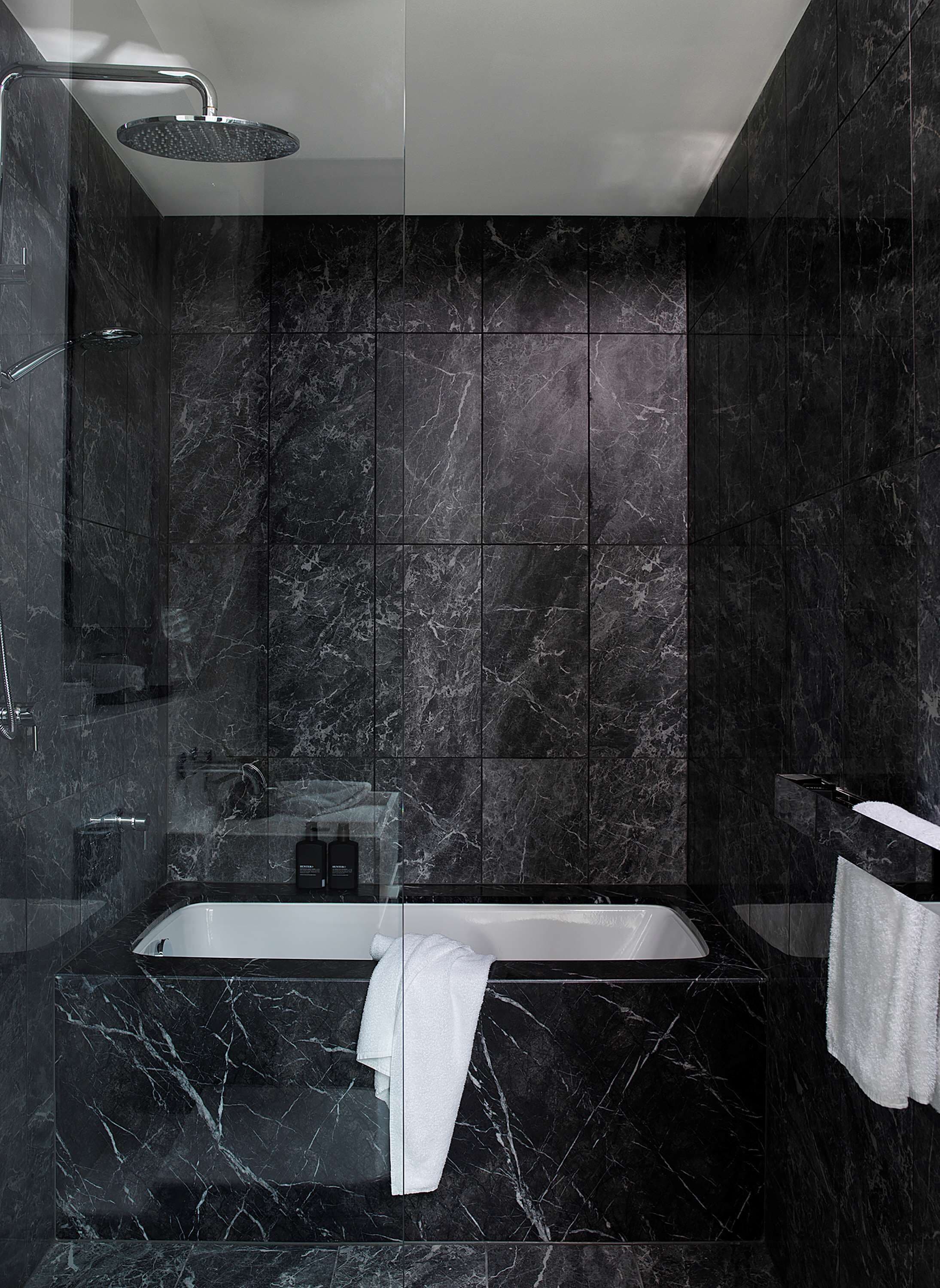 A modern bathroom with a freestanding bathtub, a glass-enclosed shower, and dark marble tiles.
