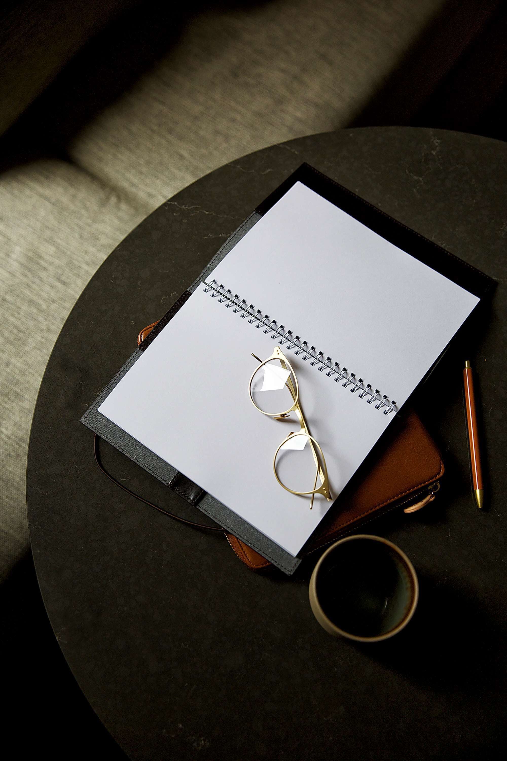 A notebook, glasses, pen, and a cup on a round table.