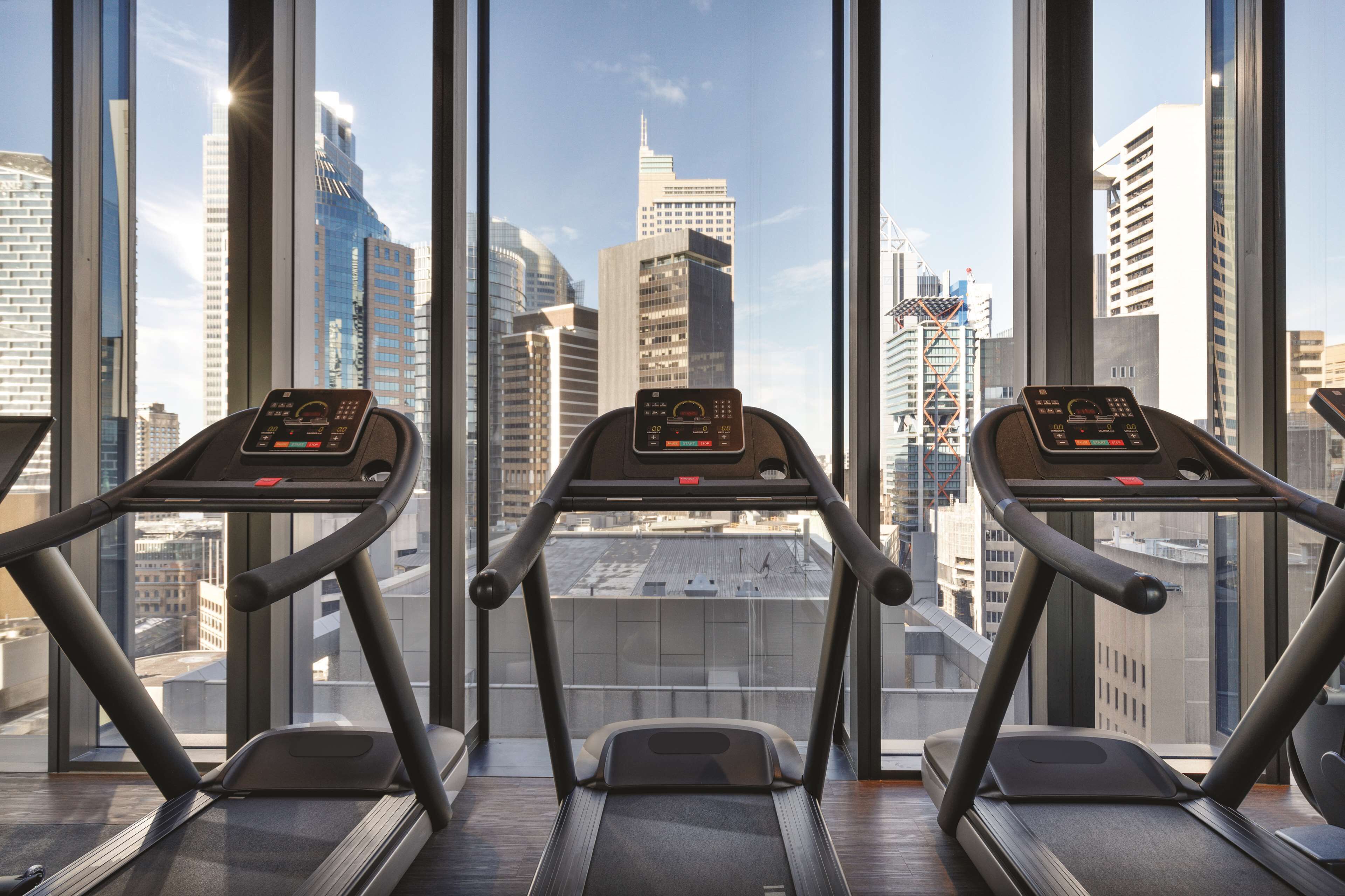 Three treadmills in a room with large windows overlooking a cityscape.