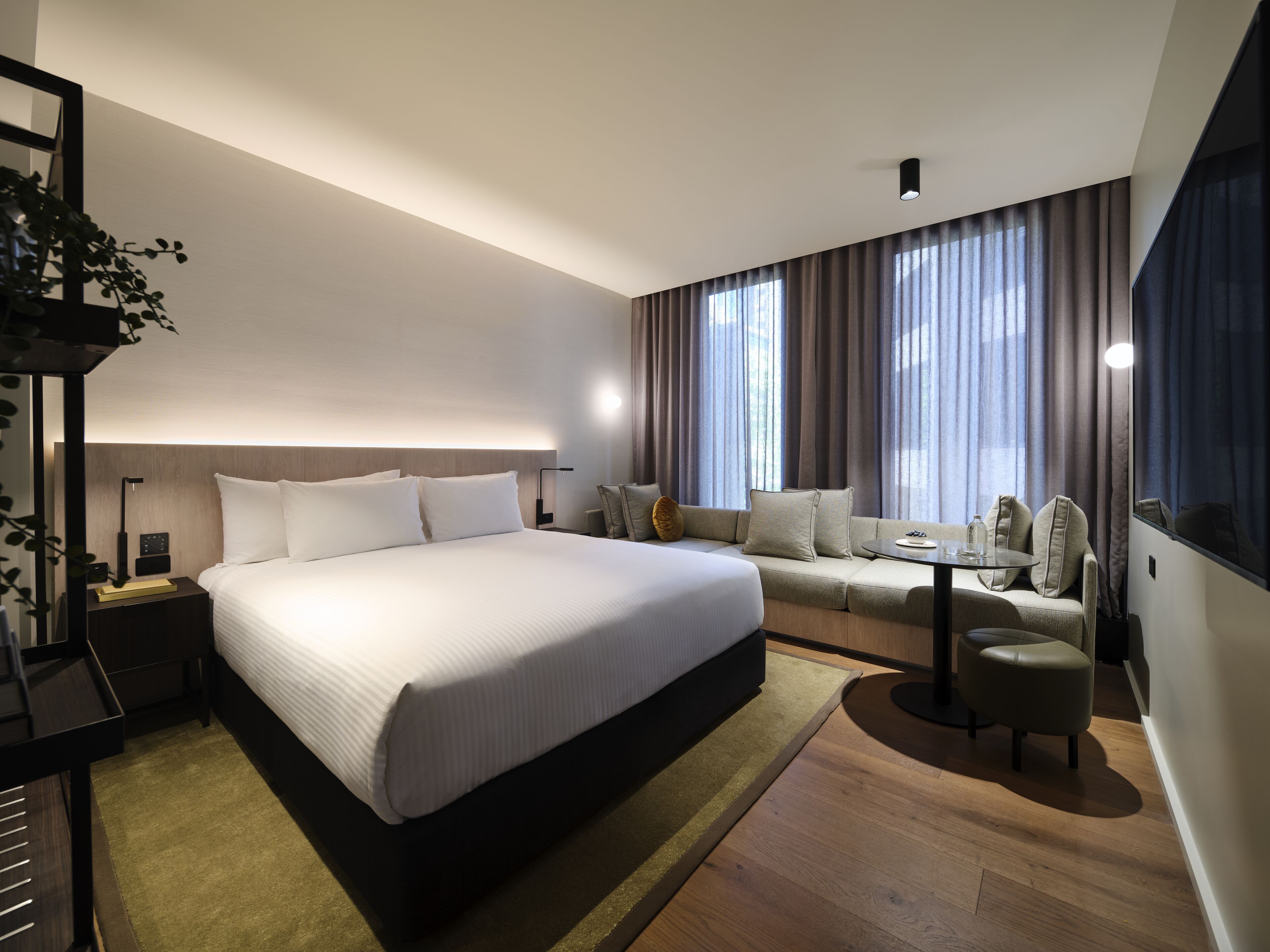 A modern hotel room with a large bed, a sofa, a small table, and a desk.