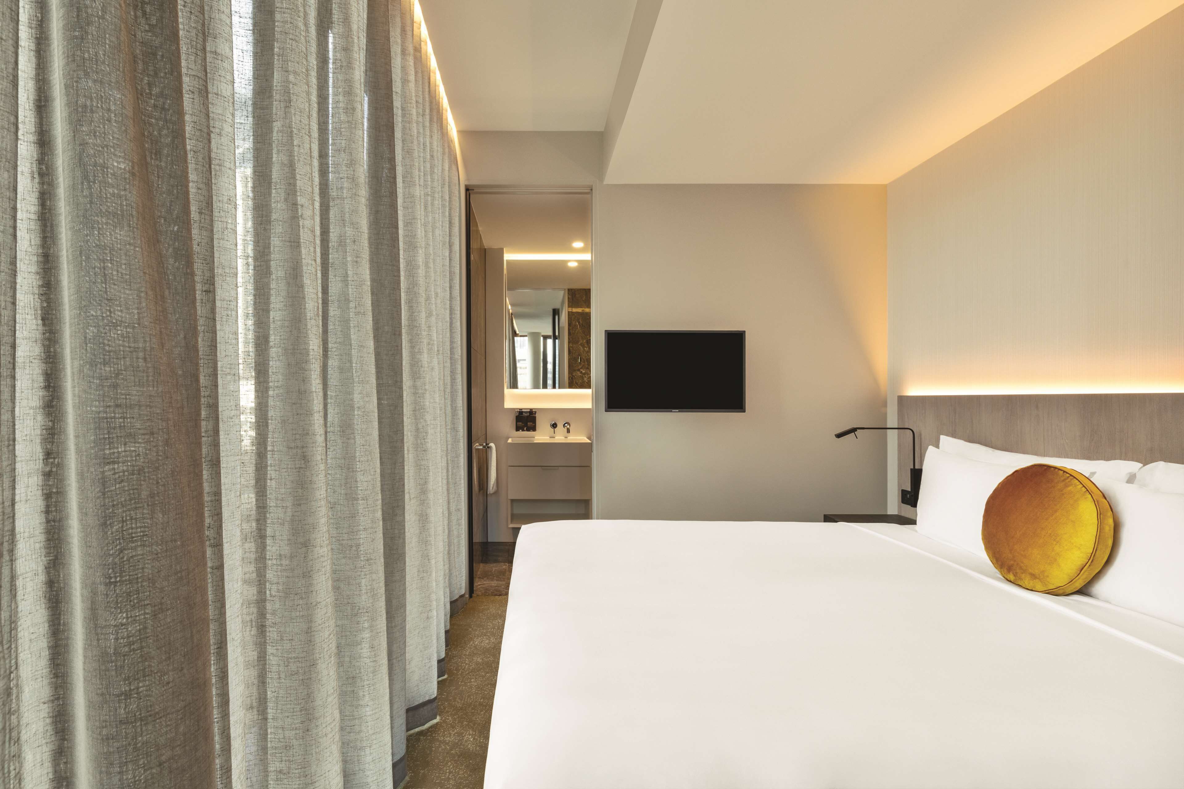 Ein Hotelzimmer mit einem großen Bett, einem wandmontierten Flachbildfernseher, einem Nachttisch und einem durch eine offene Tür einsehbaren Badezimmer.