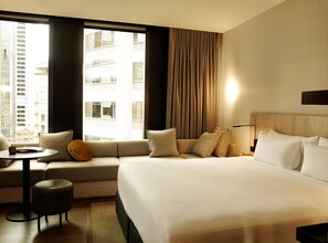 Une chambre d’hôtel avec un grand lit, un canapé, une petite table et une vue sur le paysage urbain par la fenêtre.