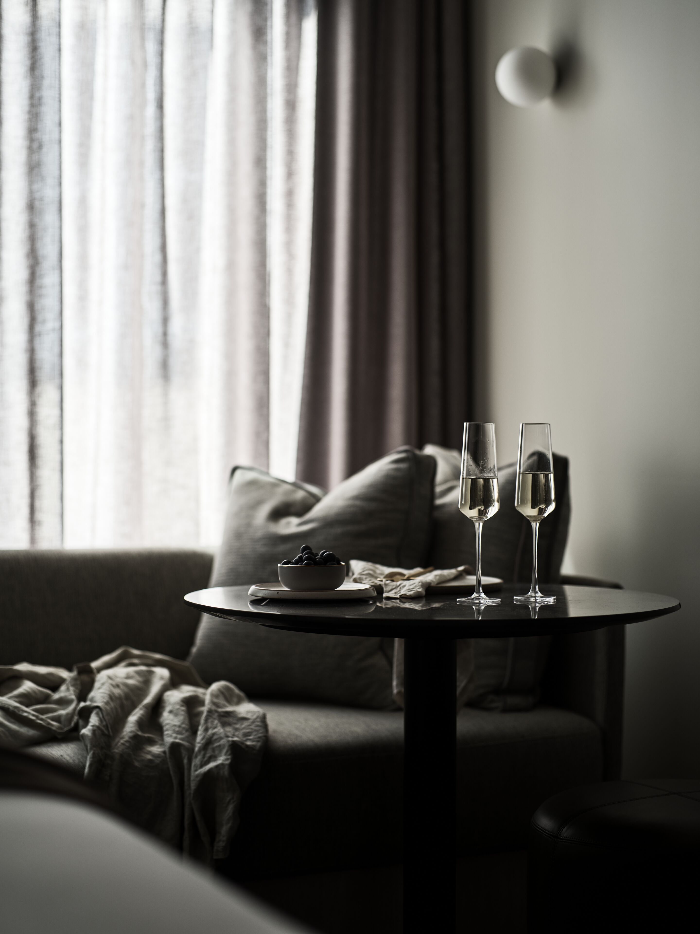 A cozy room with a round table, two glasses of champagne, a bowl of fruit, and a comfortable sofa.